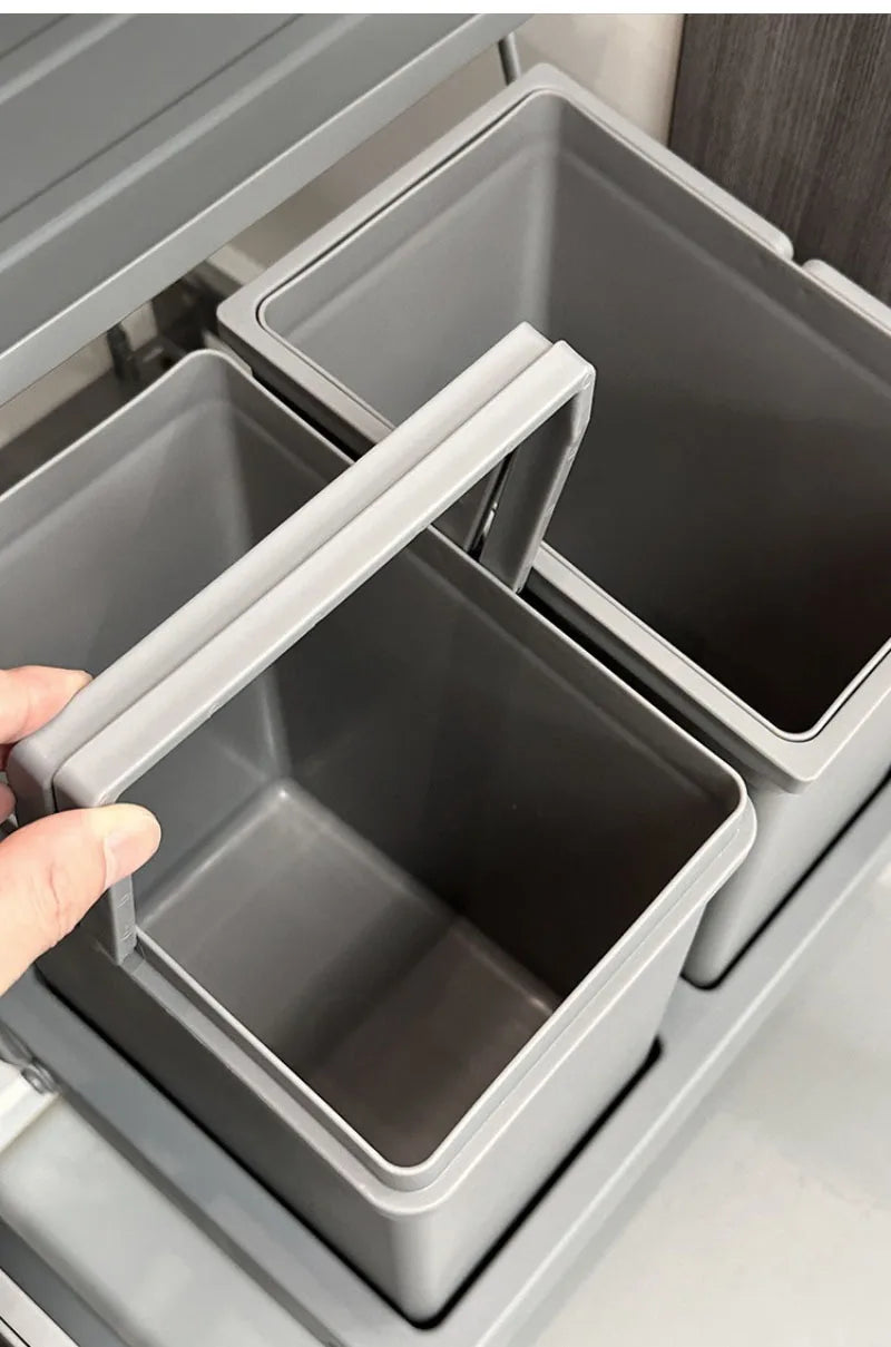 A close-up of a hand lifting a gray plastic drawer organizer bin, showing its sliding pull-out design inside a matching gray drawer.