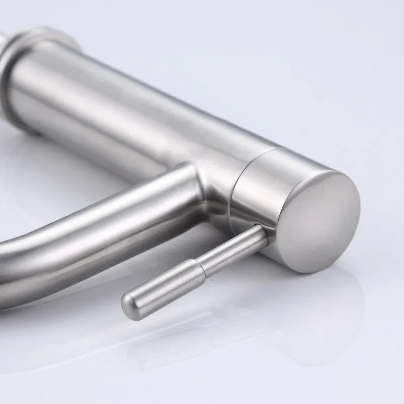 A close-up of a modern single-handle bathroom faucet with a brushed stainless steel finish, featuring a curved spout and a small side lever, shown on a reflective white surface.