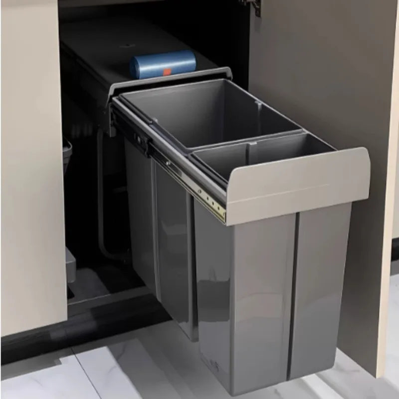 Gray pull-out trash bin inside a kitchen cabinet.