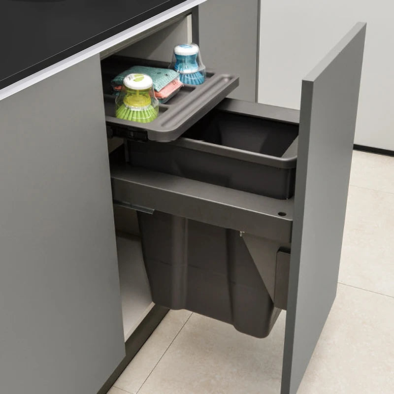 Grey kitchen cabinet with a pull-out trash bin and cleaning supplies.