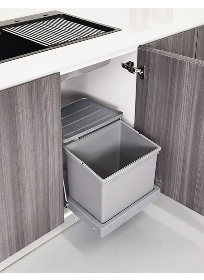 A pull-out undercounter storage bin with a gray interior and light gray outer housing, shown installed inside an open kitchen cabinet next to a sink.