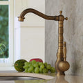 Bronze kitchen faucet on a marble countertop with grapes and a watermelon.
