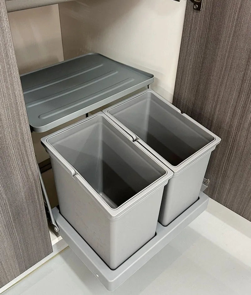 A two-bin under-cabinet pull-out trash cans system with a grey base tray and matching grey lids, shown installed inside a kitchen cabinet.