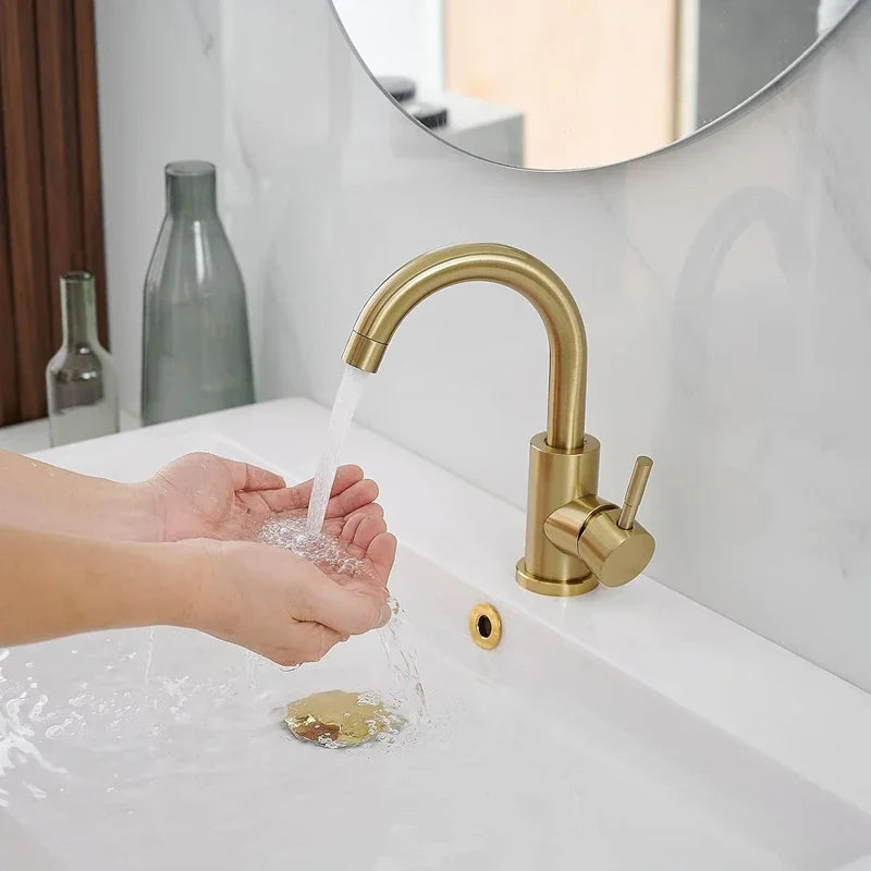 Person washing hands under a gold faucet in a bathroom setting