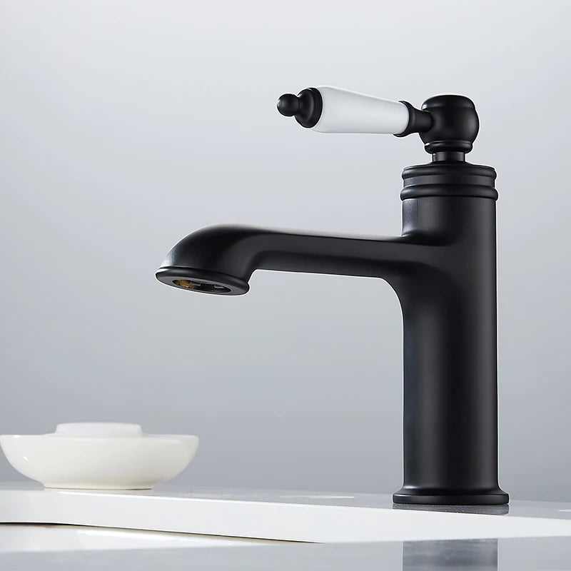 A matte black single-handle bathroom faucet with a white ceramic lever handle, mounted on a white sink against a light gray background.