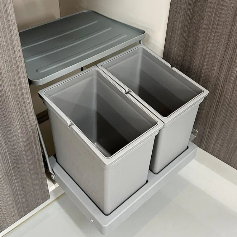 A two-compartment pull-out under-cabinet organizer bin set in a kitchen cabinet, shown with its lid resting on the upper cabinet interior.