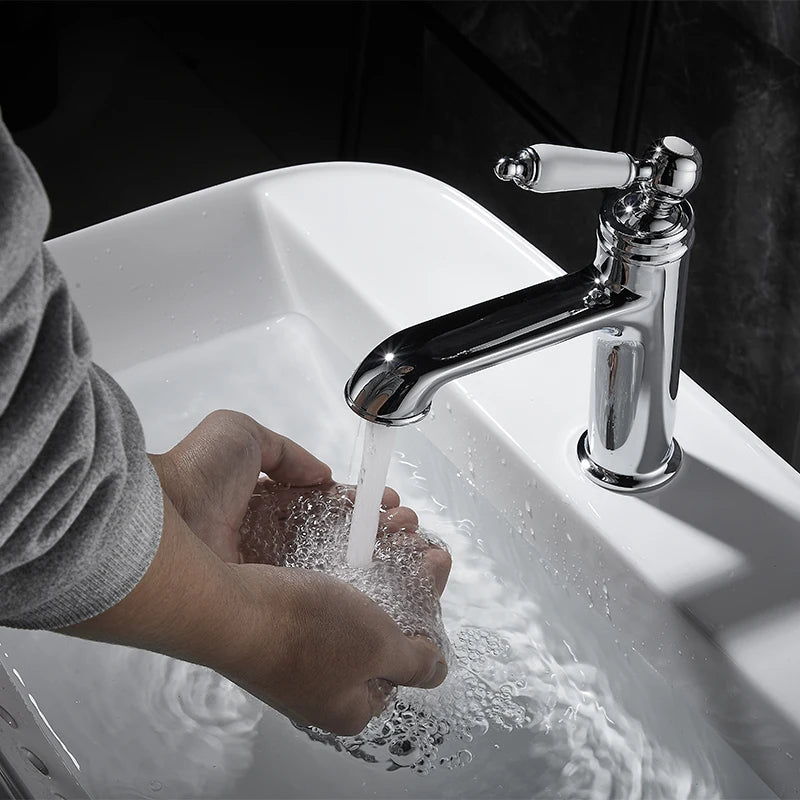 Person washing hands under a chrome faucet in a white sink.