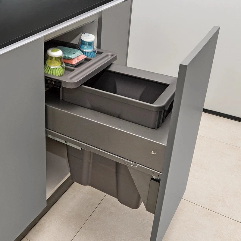 Grey kitchen cabinet with a pull-out trash bin containing cleaning supplies.