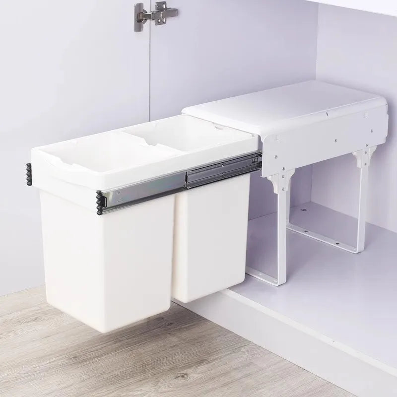 White kitchen cabinet with a pull-out trash bin on a light wood floor.