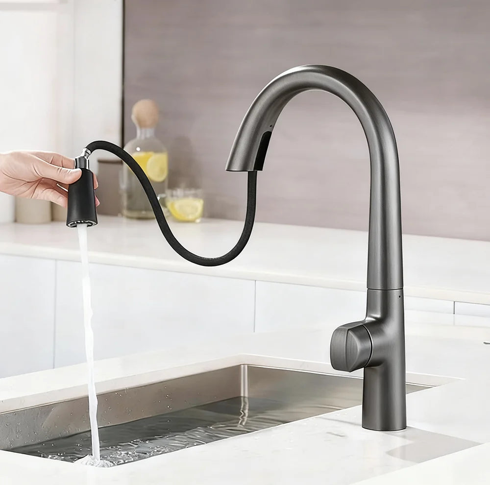 A matte black high-arc kitchen faucet with a pull-out hose and spray head, shown with water running into a sink. A hand is holding the detached spray head.