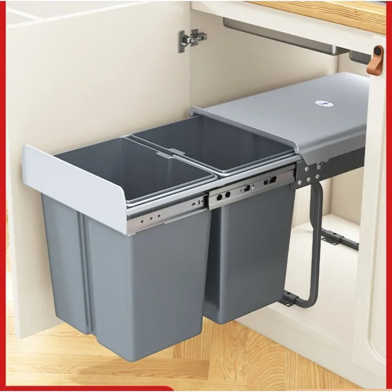 A pull-out double trash bin organizer mounted inside a kitchen cabinet, with two gray bins on metal slides and a gray lid resting on top.