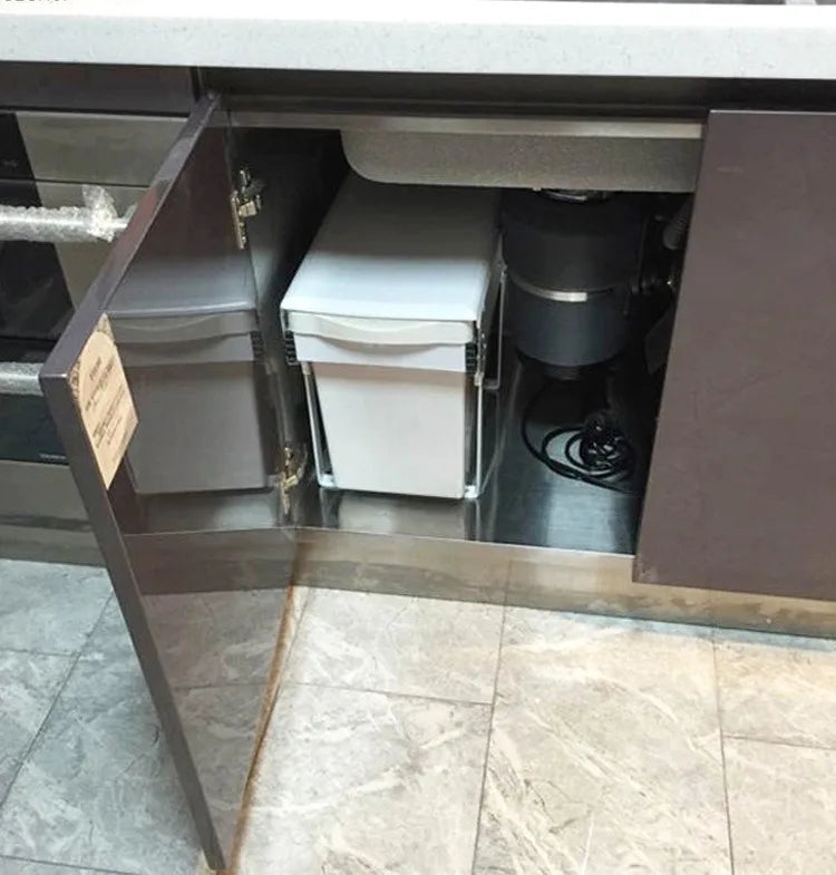 Open kitchen cabinet revealing storage bins and a trash can.