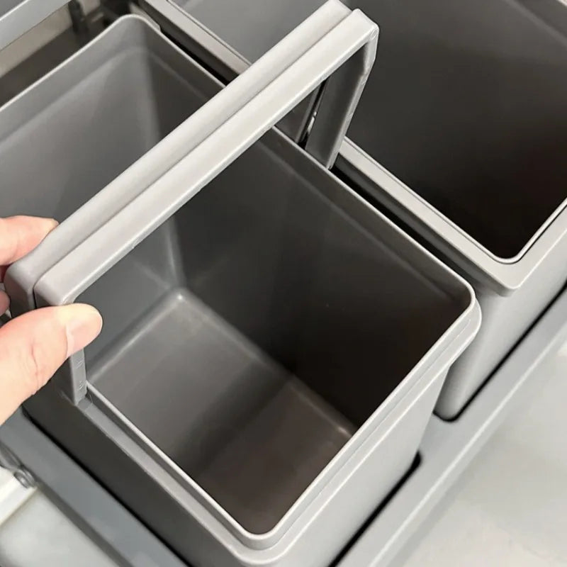 A close-up of a grey plastic drawer organizer bin with a handle being lifted by a hand, showing its interior compartment.