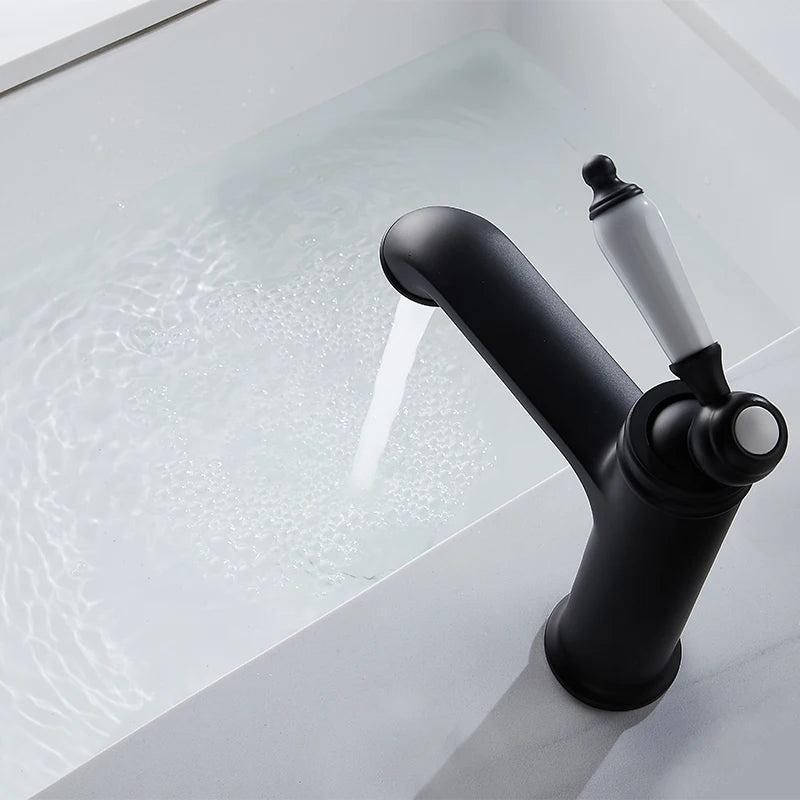 A matte black single-handle bathroom faucet with a white ceramic lever, shown with water running into a white sink.