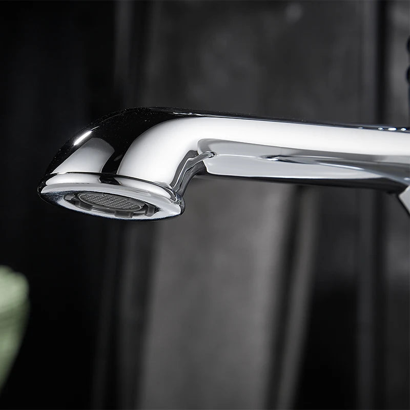 A close-up of a polished chrome faucet spout and head against a dark, blurred background.